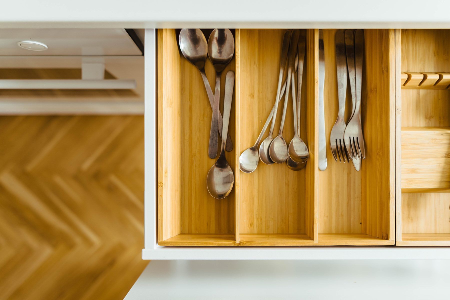 Cassetto di cucina aperto con divisori in legno chiaro e posate